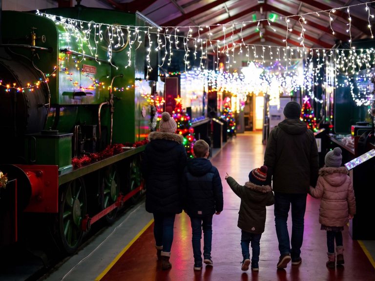 Family walking through the Display Hall decorated with Christmas lights, past a green steam engine